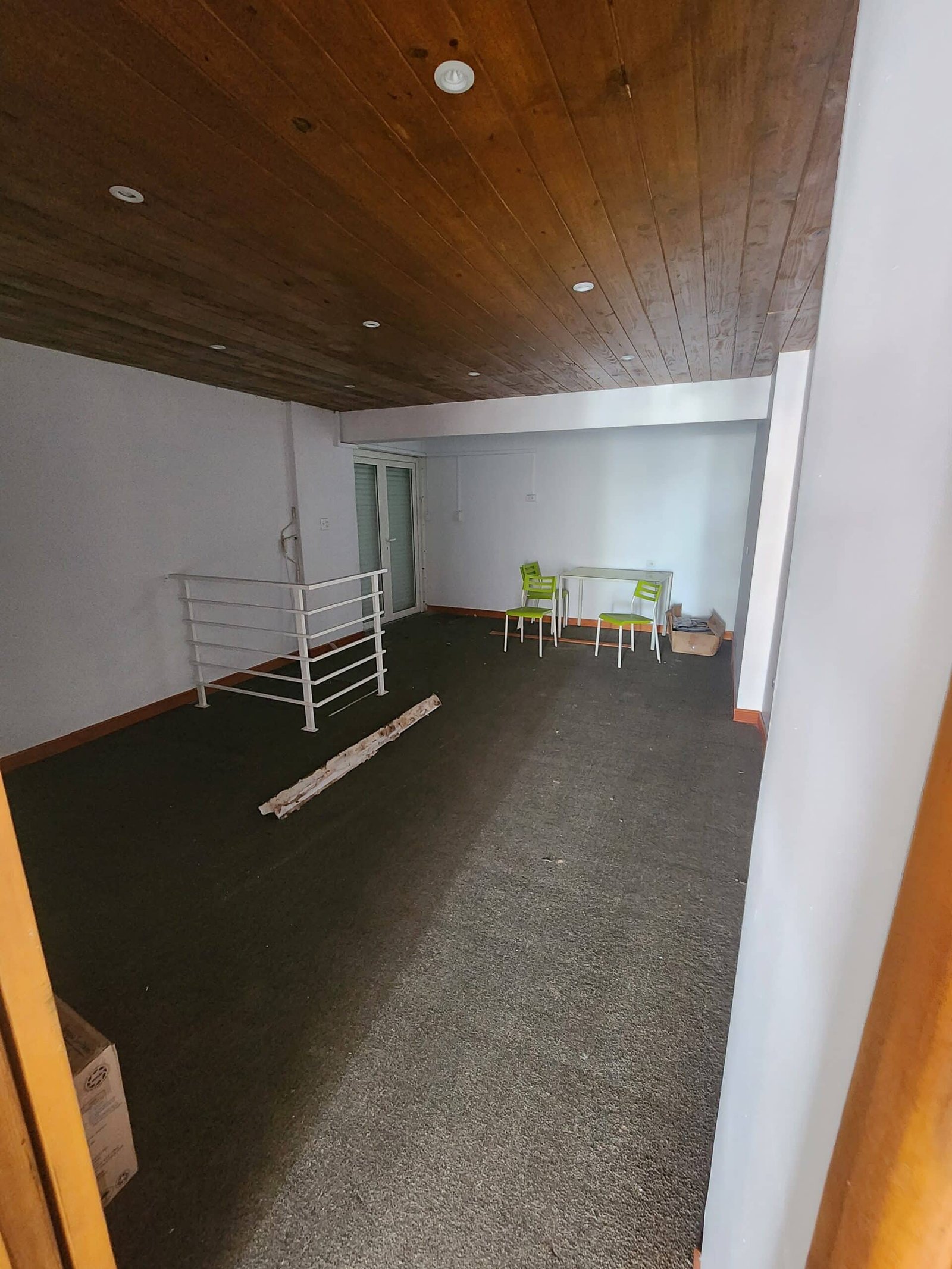 Room with a dark wooden ceiling, white walls, and a small white table surrounded by four lime‑green chairs in the corner.
