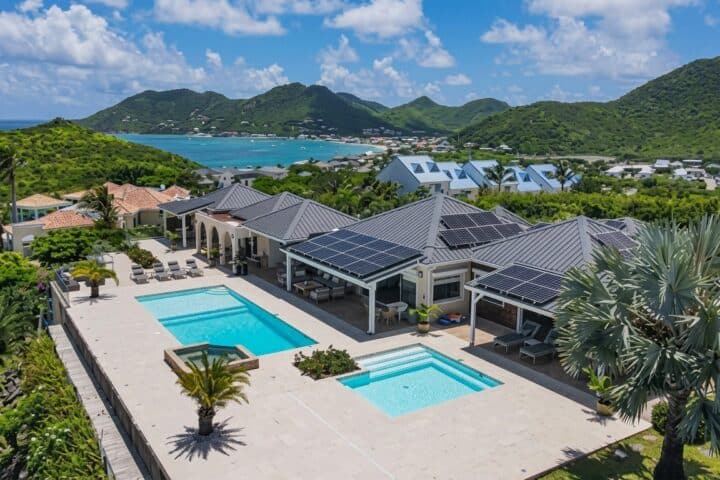 Aerial view of a luxury villa with two pools, palm trees, and solar panels on the roof." (Note: ensure this alt text is concise and without stray quotes)