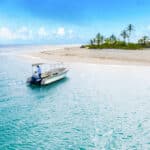 A small motorboat anchored near a sandy tropical beach with turquoise water and palm trees.