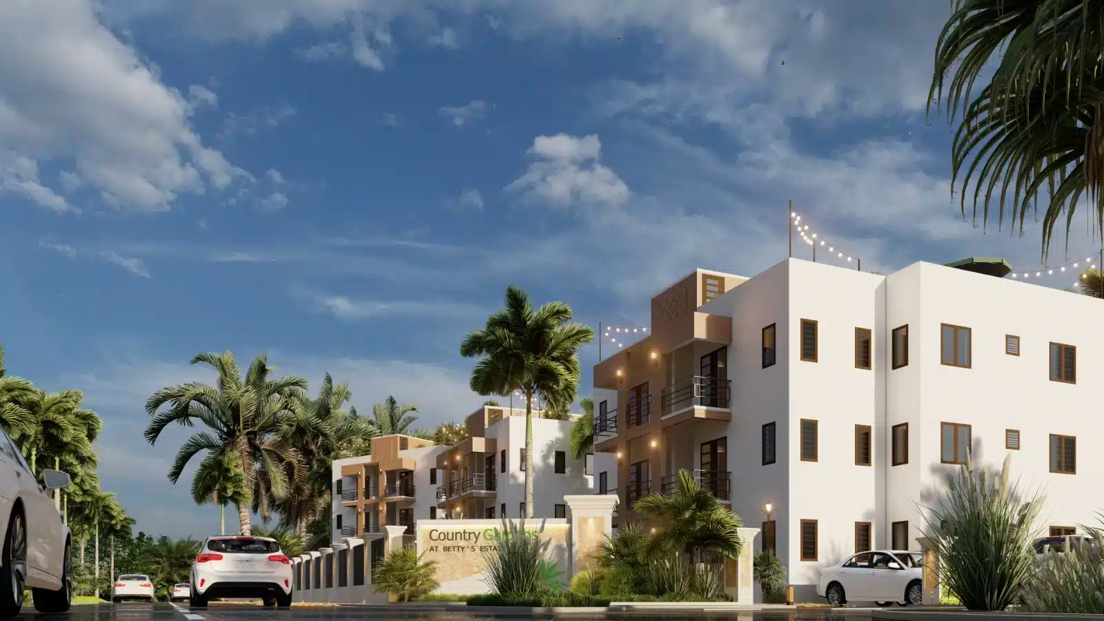 Modern white residential buildings with balconies and palm trees along a gated street at dusk, string lights overhead, several parked cars nearby