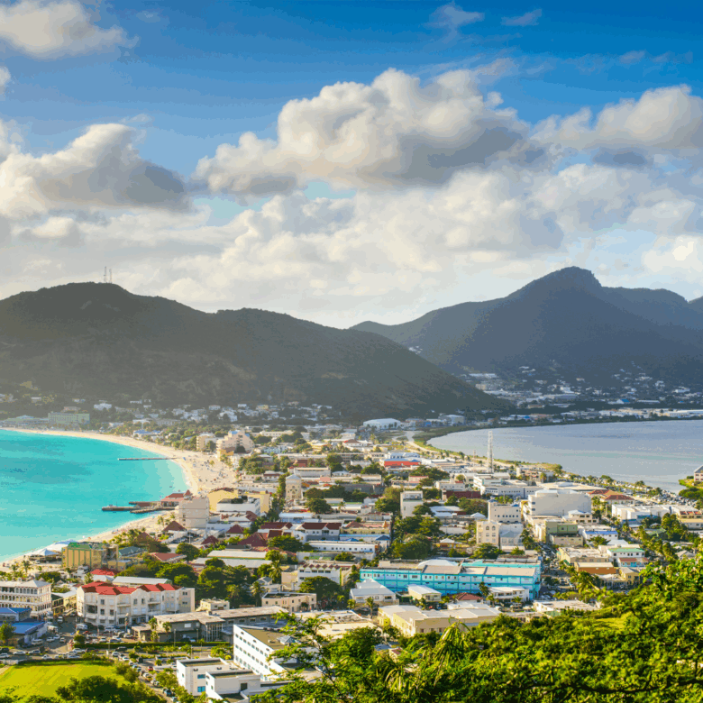 A tropical coastal town along a turquoise bay with colorful buildings and green hills in the background.