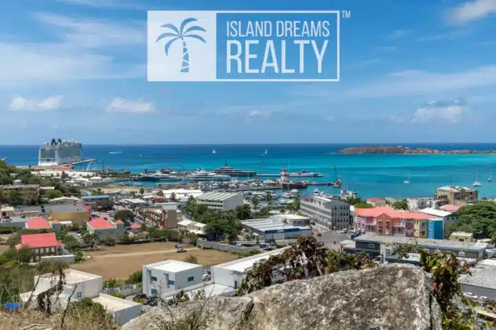 Coastal cityscape with turquoise bay, boats, and colorful buildings; a large 'Island Dreams Realty' logo overlays the sky above the scene.