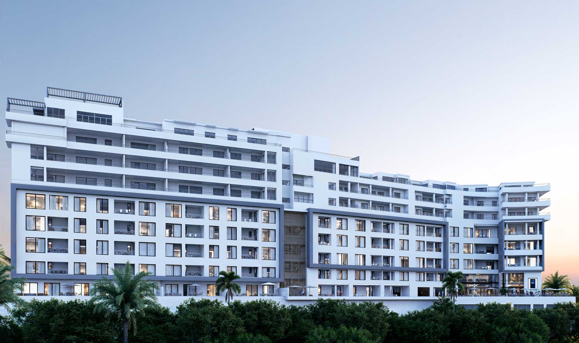 Modern white apartment building with many balconies and large windows, set against a clear blue sky with greenery in the foreground